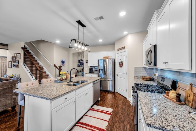 kitchen with sink, white cabinetry, a center island with sink, stainless steel appliances, and a kitchen bar