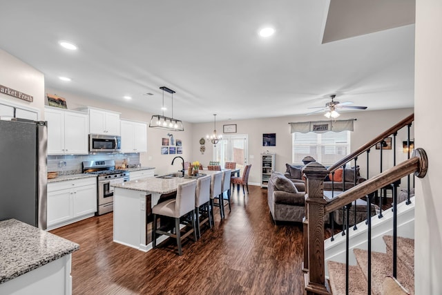 kitchen with appliances with stainless steel finishes, hanging light fixtures, light stone countertops, white cabinets, and a center island with sink