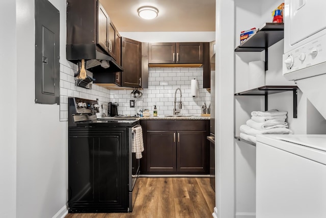 kitchen featuring sink, black range with electric stovetop, backsplash, electric panel, and stacked washer / dryer