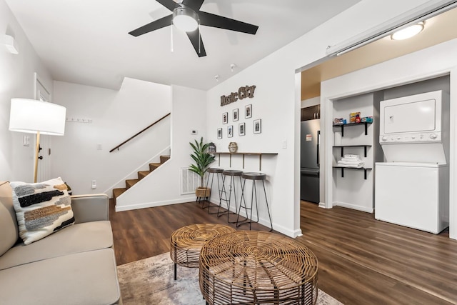 living room featuring stacked washer / drying machine, dark wood-type flooring, and ceiling fan