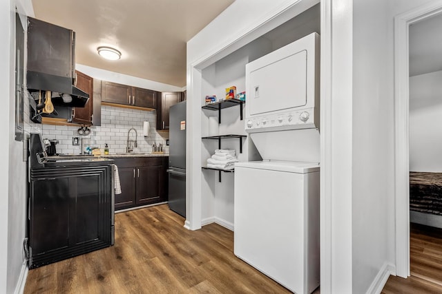 kitchen featuring stacked washer and clothes dryer, sink, dark hardwood / wood-style floors, black range with electric cooktop, and backsplash