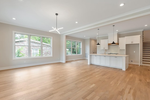 kitchen featuring pendant lighting, sink, white cabinets, backsplash, and a kitchen island with sink