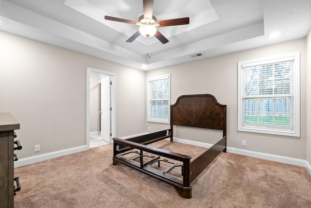 carpeted bedroom with ensuite bathroom, ceiling fan, and a tray ceiling