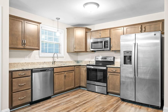 kitchen featuring sink, light stone counters, hanging light fixtures, stainless steel appliances, and light hardwood / wood-style floors