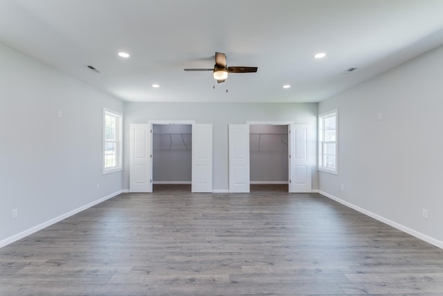 unfurnished bedroom featuring multiple closets, ceiling fan, hardwood / wood-style floors, and multiple windows