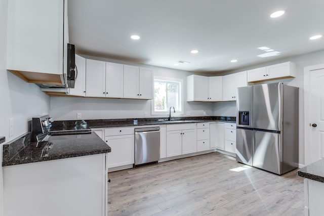 kitchen featuring sink, appliances with stainless steel finishes, dark stone counters, light hardwood / wood-style floors, and white cabinets