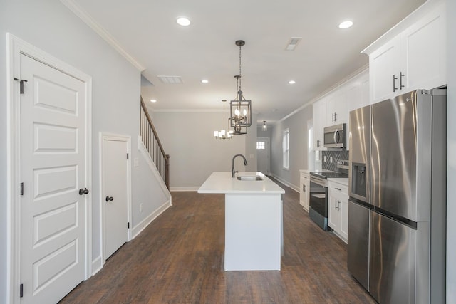 kitchen with appliances with stainless steel finishes, white cabinetry, sink, hanging light fixtures, and a center island with sink