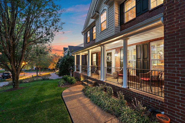 property exterior at dusk with a porch and a lawn