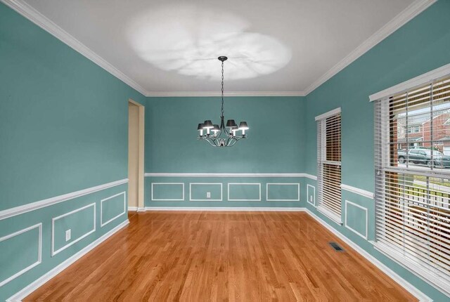 unfurnished dining area with an inviting chandelier, hardwood / wood-style floors, and crown molding