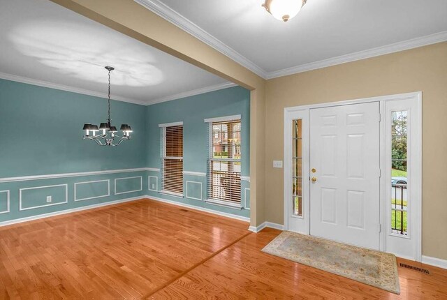 entrance foyer featuring hardwood / wood-style flooring, ornamental molding, and a chandelier