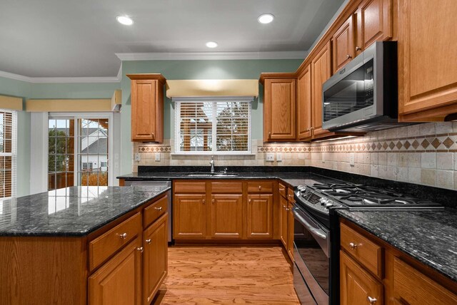 kitchen featuring sink, ornamental molding, dark stone counters, gas range oven, and light hardwood / wood-style floors