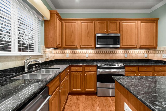 kitchen with stainless steel appliances, ornamental molding, sink, and dark stone countertops