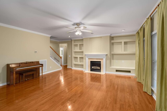 unfurnished living room featuring built in shelves, ceiling fan, crown molding, and light hardwood / wood-style floors