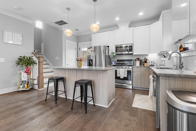 kitchen with sink, appliances with stainless steel finishes, white cabinetry, a center island, and decorative light fixtures