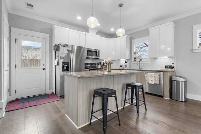 kitchen with a breakfast bar area, white cabinetry, stainless steel appliances, a kitchen island, and decorative light fixtures