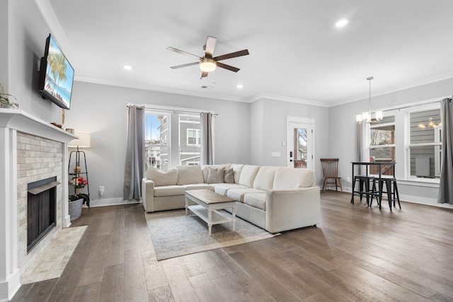 living room with crown molding, a brick fireplace, hardwood / wood-style floors, and ceiling fan with notable chandelier