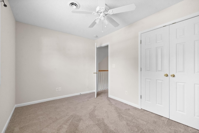 unfurnished bedroom with ceiling fan, light colored carpet, a closet, and a textured ceiling