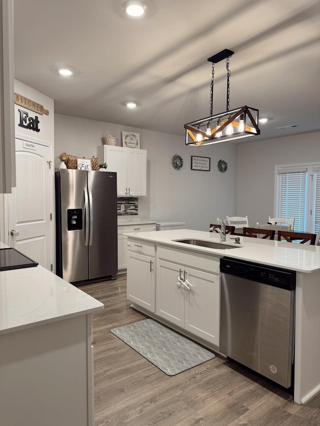 kitchen with sink, appliances with stainless steel finishes, pendant lighting, a kitchen island with sink, and white cabinets