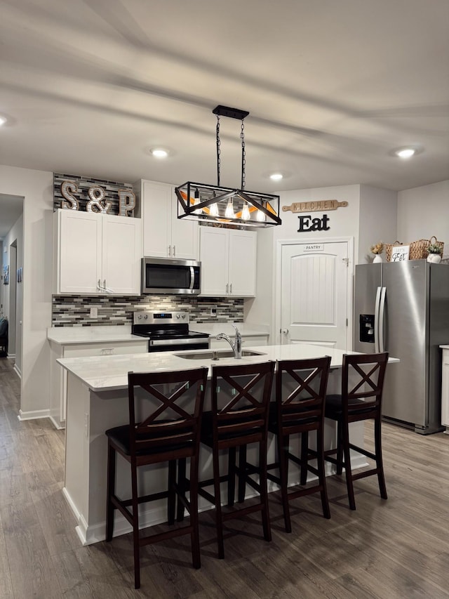 kitchen featuring white cabinetry, decorative light fixtures, dark hardwood / wood-style floors, stainless steel appliances, and a kitchen island with sink