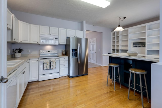 kitchen with white appliances, a kitchen breakfast bar, light hardwood / wood-style floors, white cabinets, and decorative light fixtures