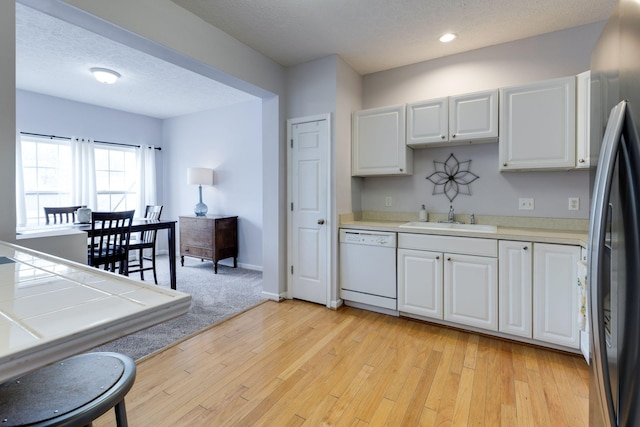 kitchen with sink, white cabinetry, black fridge, light hardwood / wood-style flooring, and dishwasher