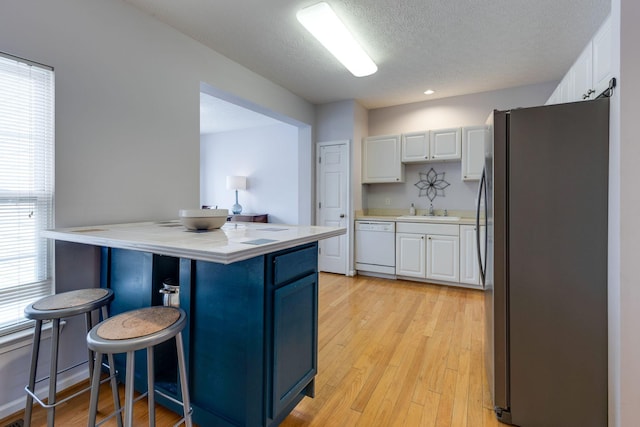 kitchen featuring a breakfast bar, white cabinets, stainless steel fridge, white dishwasher, and light hardwood / wood-style flooring