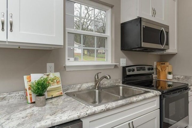 kitchen featuring sink, stainless steel appliances, white cabinetry, and light stone counters