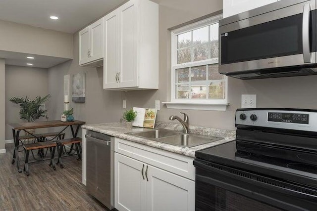 kitchen featuring appliances with stainless steel finishes, sink, light stone counters, white cabinetry, and dark hardwood / wood-style floors