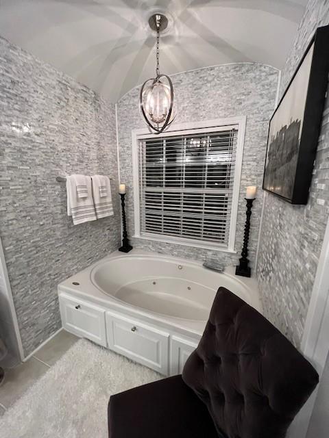 bathroom featuring an inviting chandelier, a tub to relax in, tile patterned floors, and lofted ceiling