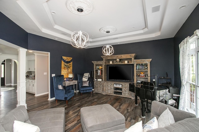 living room featuring arched walkways, decorative columns, wood finished floors, and a raised ceiling