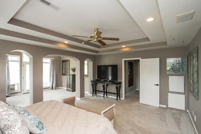 bedroom featuring arched walkways, visible vents, light colored carpet, and a tray ceiling