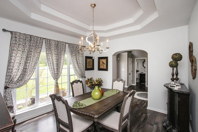 dining area with an inviting chandelier, a raised ceiling, wood finished floors, arched walkways, and a wealth of natural light