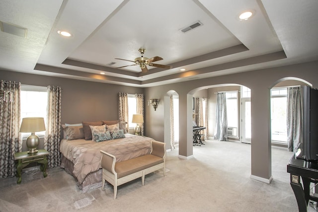 bedroom featuring multiple windows, visible vents, a tray ceiling, and arched walkways