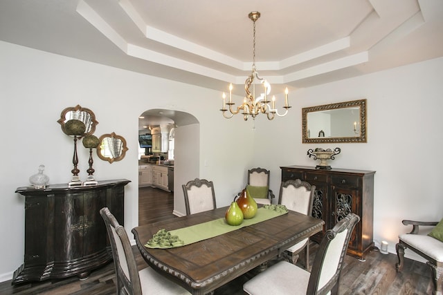 dining area with arched walkways, dark wood-style flooring, a chandelier, and a raised ceiling