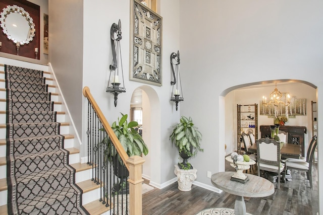 stairway featuring arched walkways, an inviting chandelier, a high ceiling, and wood finished floors
