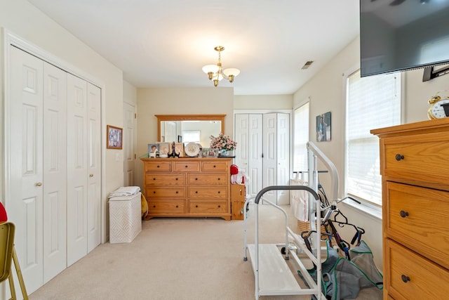 bedroom featuring light colored carpet, a notable chandelier, and multiple closets