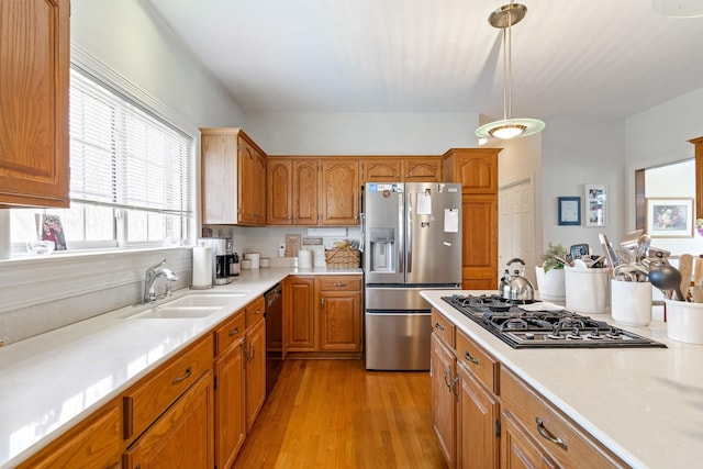 kitchen with appliances with stainless steel finishes, sink, pendant lighting, and light wood-type flooring