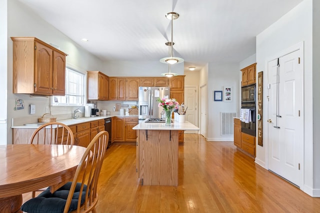 kitchen with a center island, light hardwood / wood-style flooring, black appliances, sink, and pendant lighting