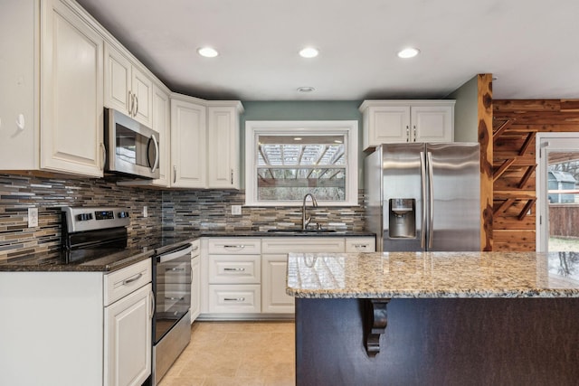 kitchen with sink, dark stone countertops, plenty of natural light, appliances with stainless steel finishes, and white cabinets