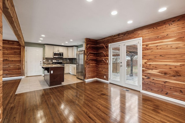 kitchen featuring appliances with stainless steel finishes, a center island, a kitchen bar, french doors, and wood walls