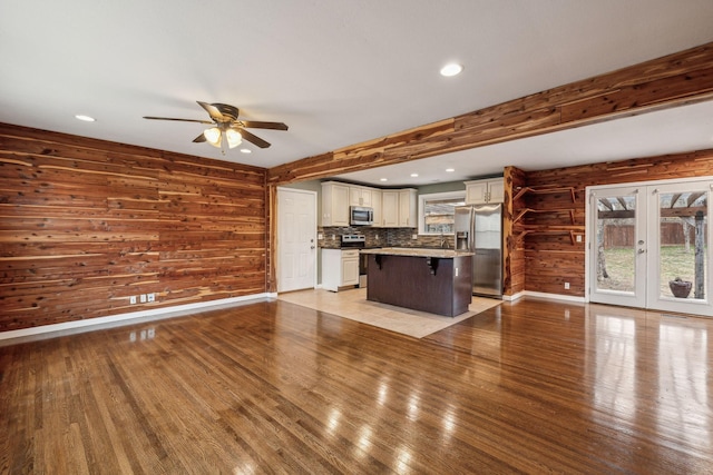 unfurnished living room with ceiling fan, light wood-type flooring, beam ceiling, and french doors