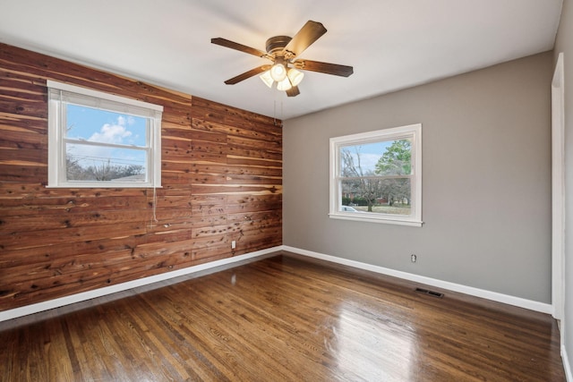 unfurnished room with wooden walls, dark hardwood / wood-style floors, and ceiling fan