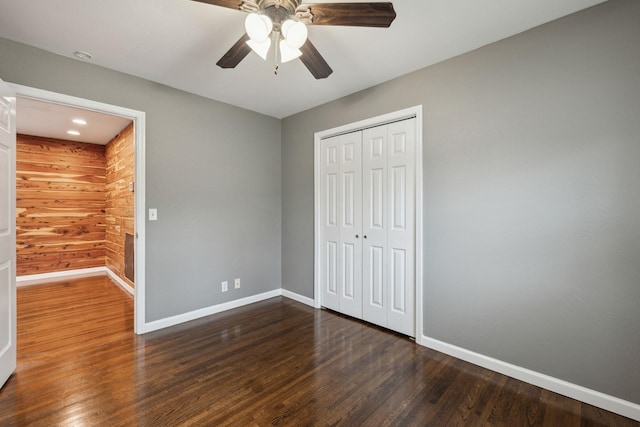 unfurnished bedroom with wooden walls, ceiling fan, dark hardwood / wood-style flooring, and a closet