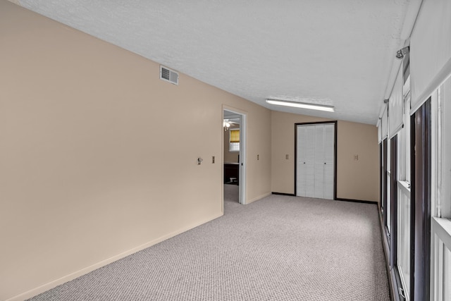 carpeted spare room featuring vaulted ceiling and a textured ceiling