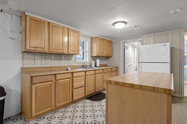 kitchen with sink, wood counters, white refrigerator, a kitchen island, and light brown cabinetry