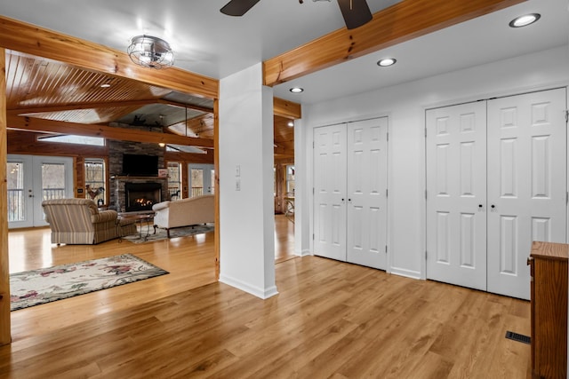 interior space with light hardwood / wood-style flooring, a fireplace, lofted ceiling with beams, and ceiling fan