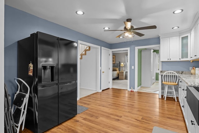 kitchen featuring white cabinetry, light hardwood / wood-style flooring, light stone counters, and black refrigerator with ice dispenser