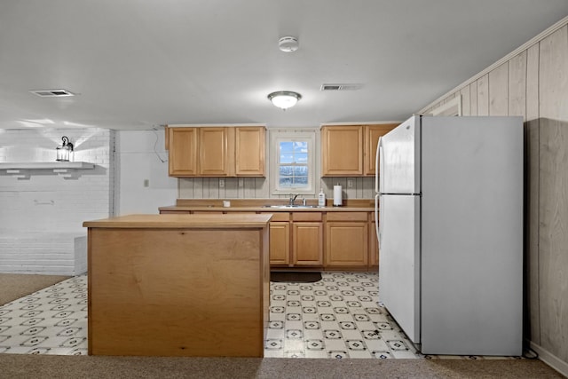 kitchen with light brown cabinetry, refrigerator, and sink