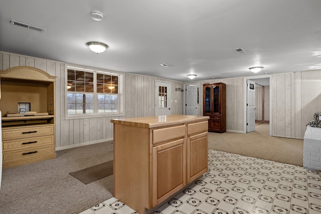 kitchen featuring light carpet, light brown cabinetry, wood walls, and a kitchen island