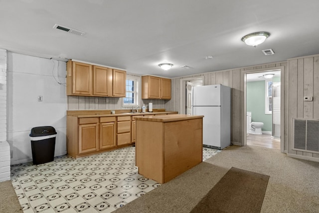 kitchen with white refrigerator, sink, a kitchen island, and light brown cabinets